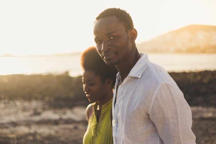 Young Man And Woman Standing On Sand Against Lake