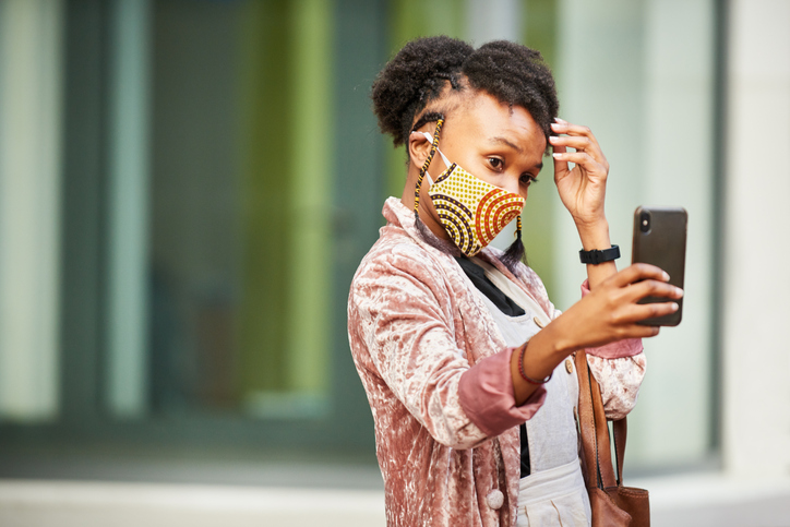 Young woman in a face mask taking selfies on a city street