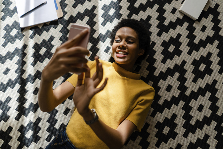 Young woman lying on carpet using smartphone