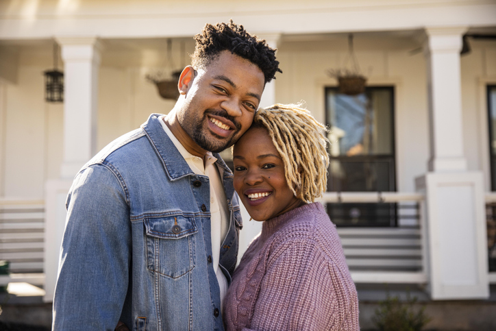 Portrait of husband and wife embracing in front of home